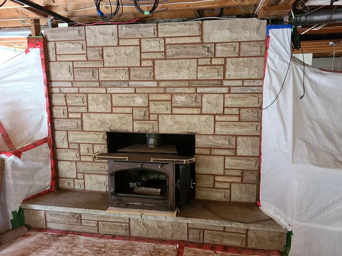Interior stone fireplace surround under construction around a wood stove