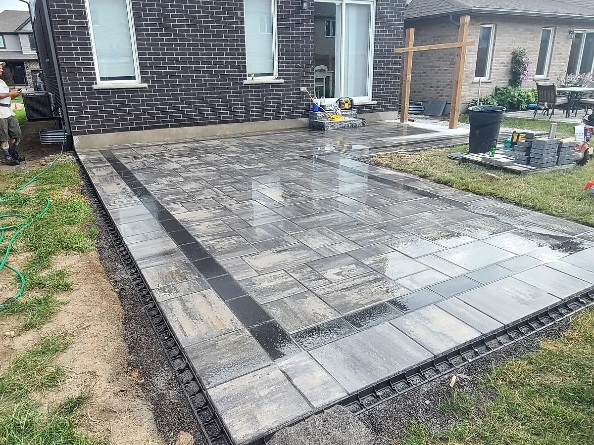 Large grey interlock paver patio laid behind a brick home