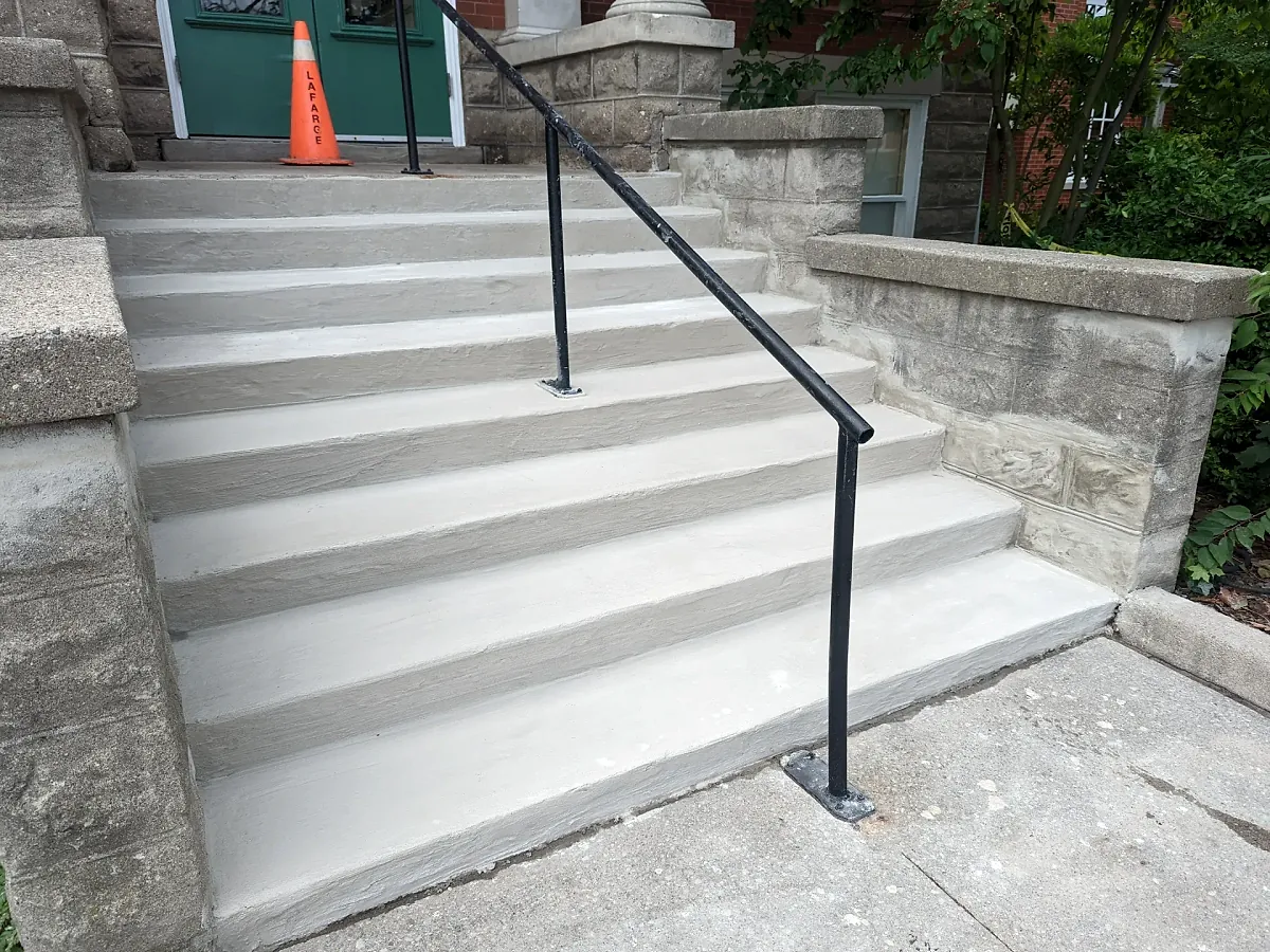 Wide poured concrete front steps with a black metal handrail