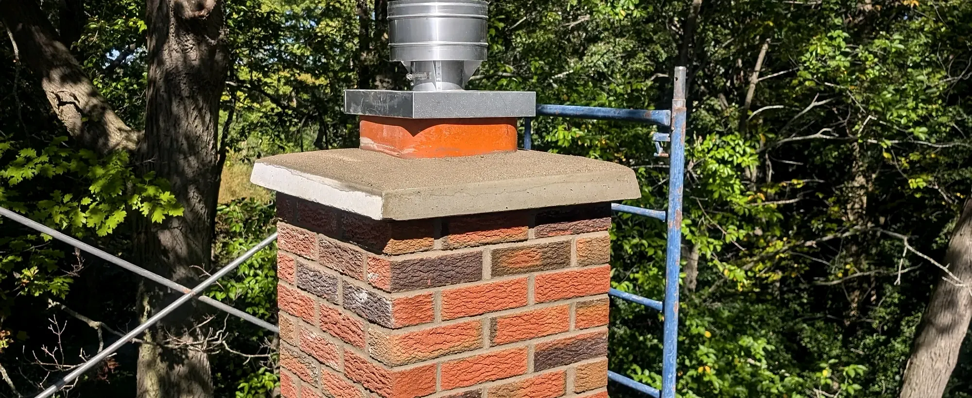 Rebuilt red brick chimney with a new concrete crown and stainless cap